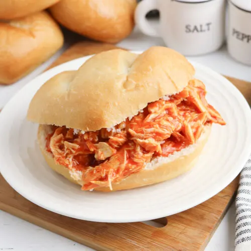 Buffalo Chicken Sandwich served on white plate on top of wooden platter.