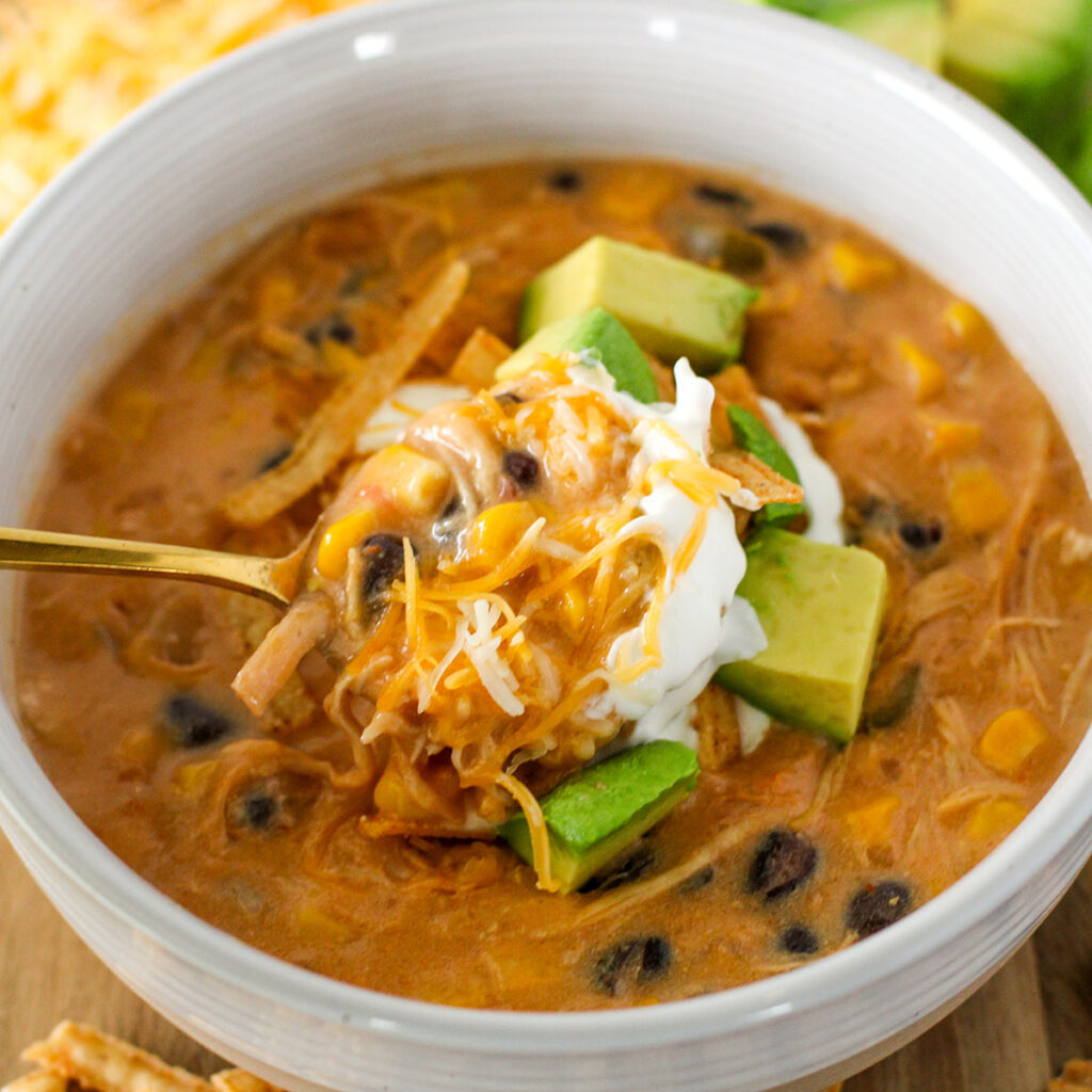 Chicken Tortilla Soup served in a bowl topped with sour cream, shredded cheese, and avocado.