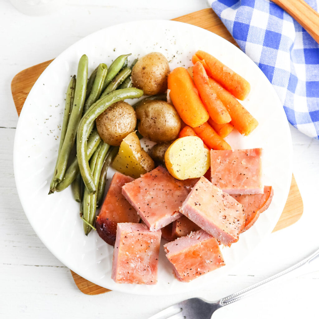 Ham, potatoes, carrots and green beans served on white plate.