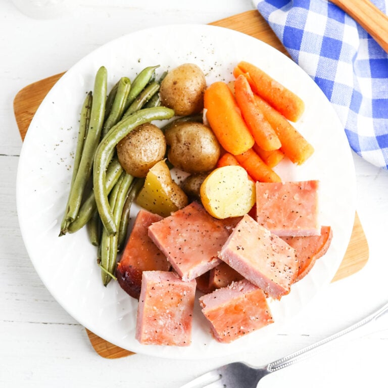 Ham, potatoes, carrots and green beans served on white plate.