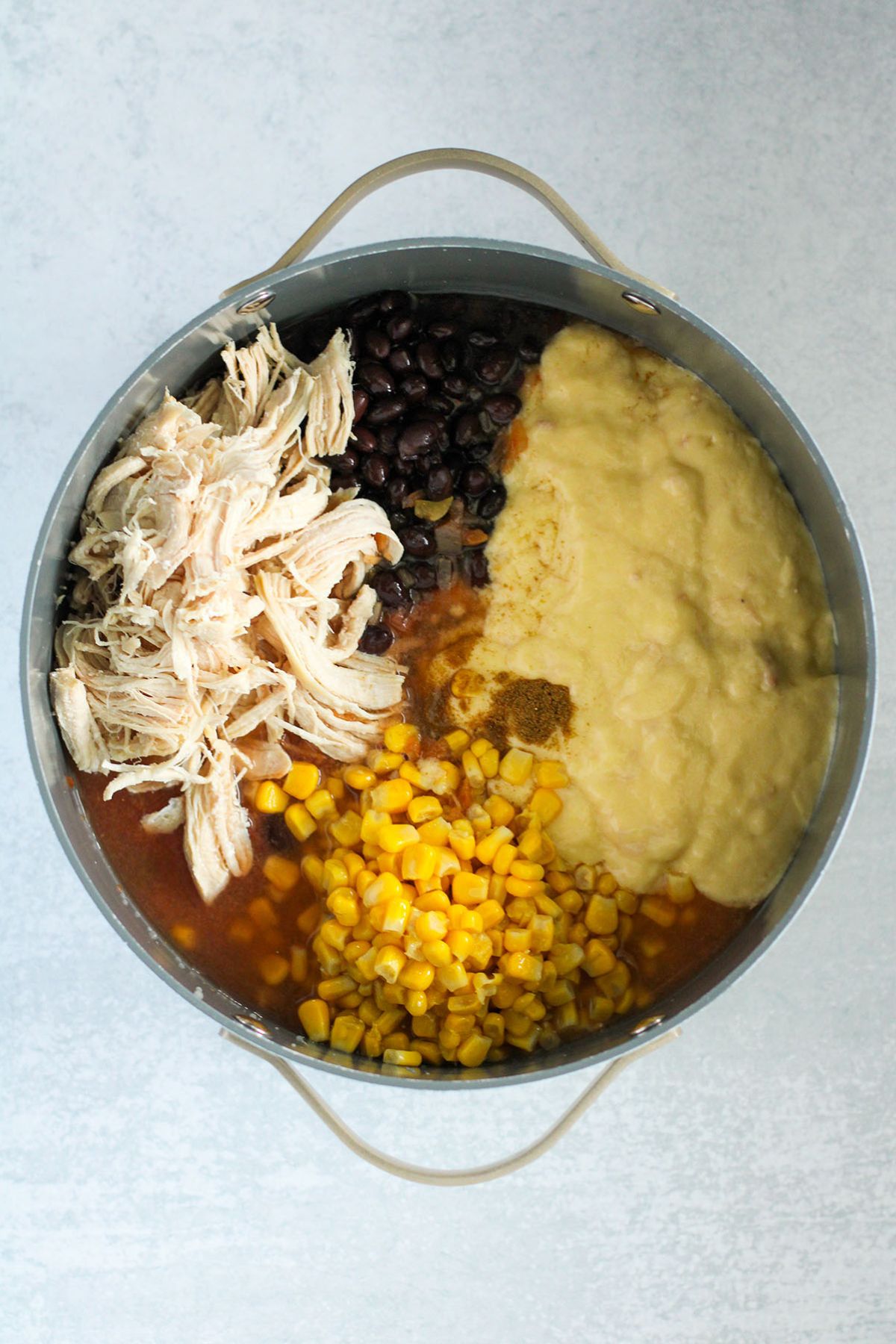 Shredded chicken, Picante sauce, cream of chicken soup, corn, black beans, water, and cumin in a large pot.