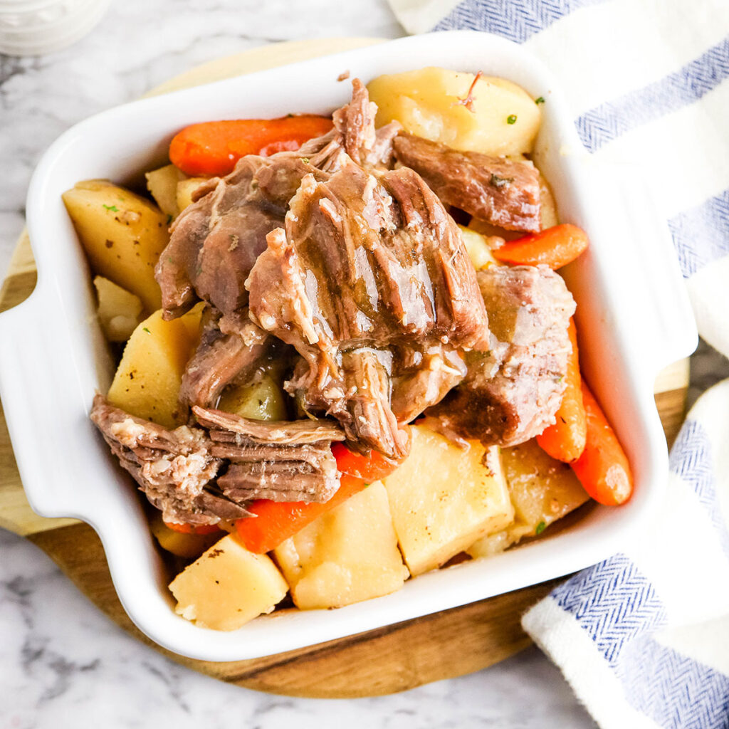 Pot Roast with potatoes and carrots in white serving dish.