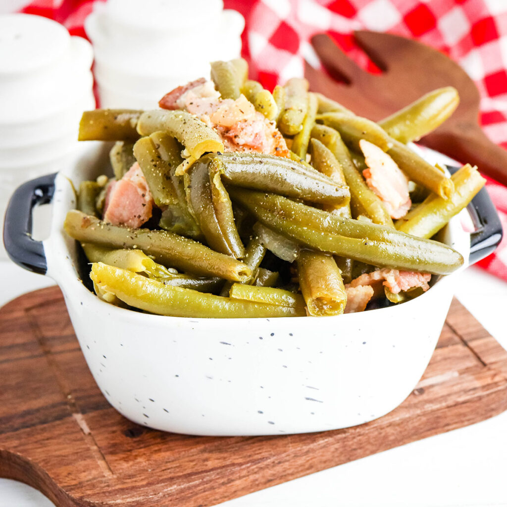 Green Beans in white serving bowl on wooden platter.