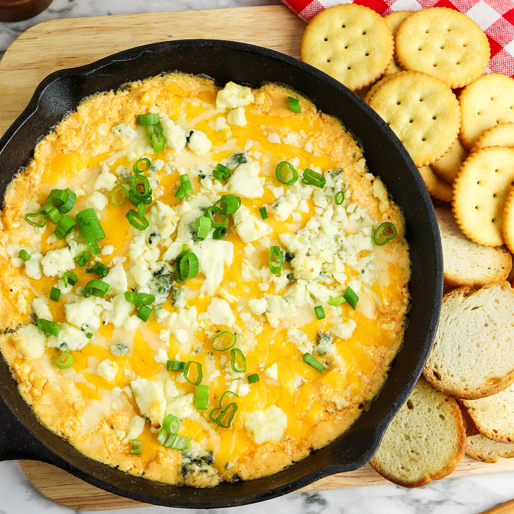 Buffalo Chicken Dip in a cast iron skillet set on a wooden board.