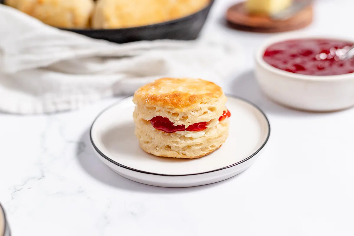 Buttermilk Biscuit with butter and strawberry jam on white plate.
