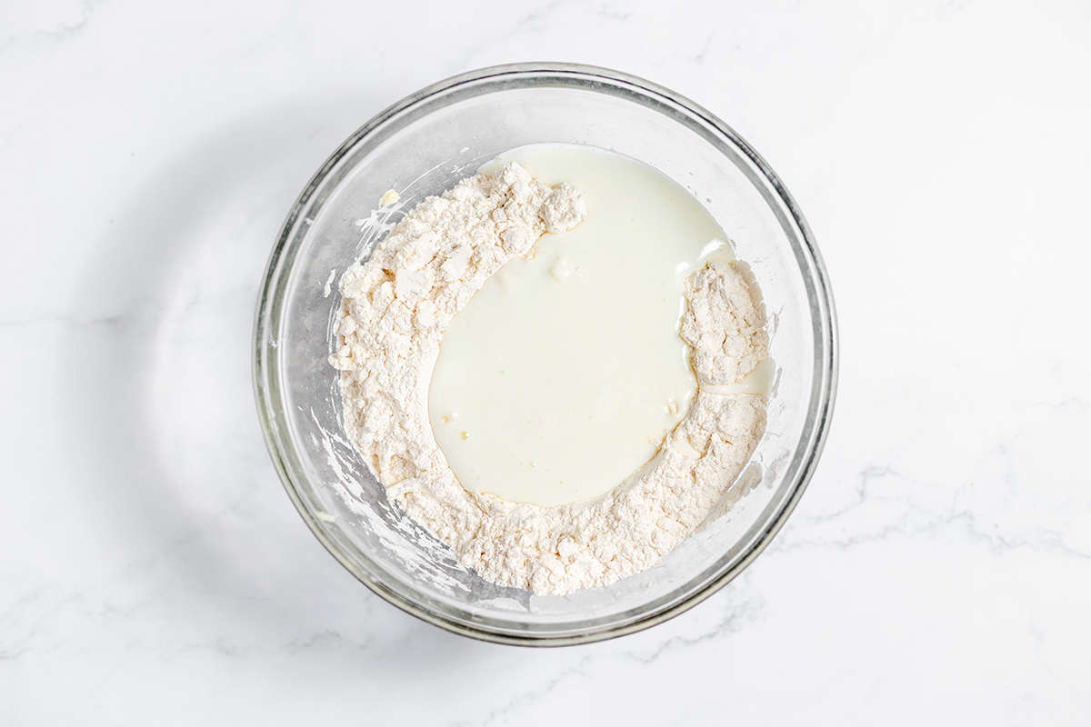 Buttermilk added to dry ingredients in glass mixing bowl.