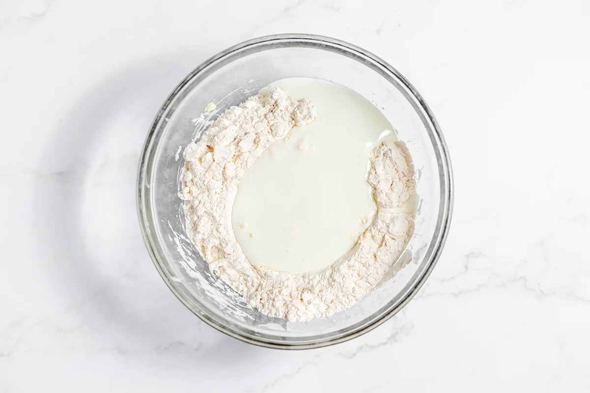 Buttermilk added to dry ingredients in glass mixing bowl.