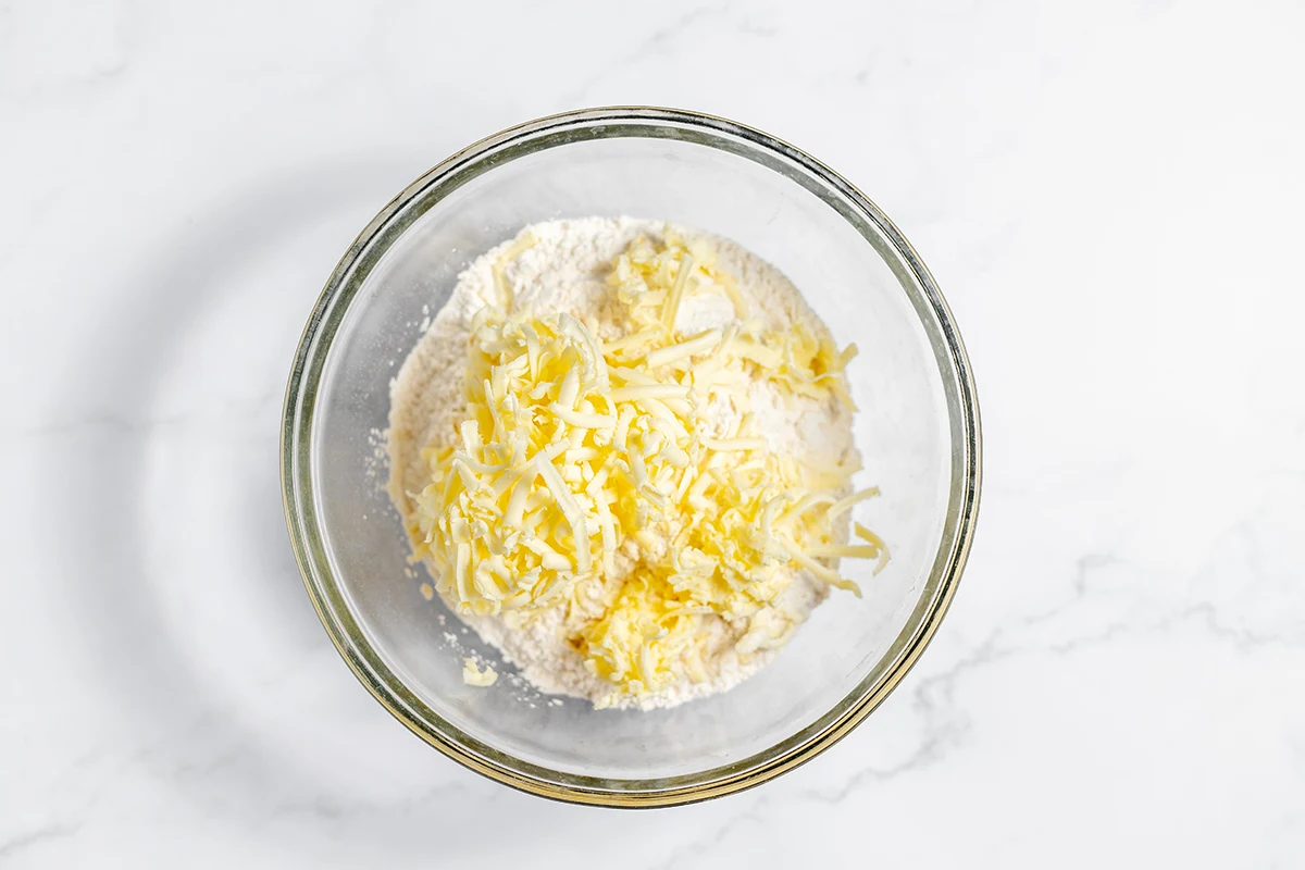 Grated butter and flour in glass mixing bowl.