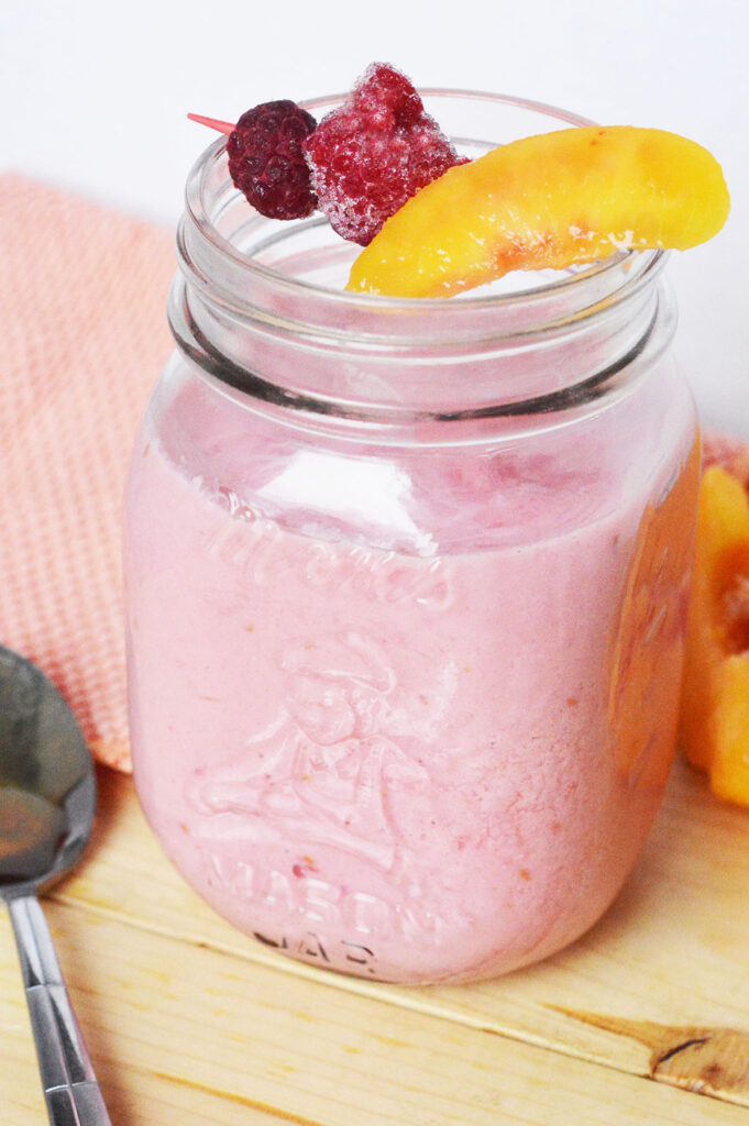 Raspberry Peach Smoothie in mason jar glass on wooden counter.