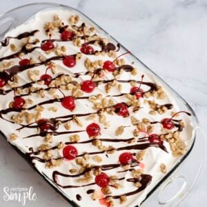 Banana Split Dessert Recipe in glass serving dish topped with cherries and drizzled with chocolate syrup