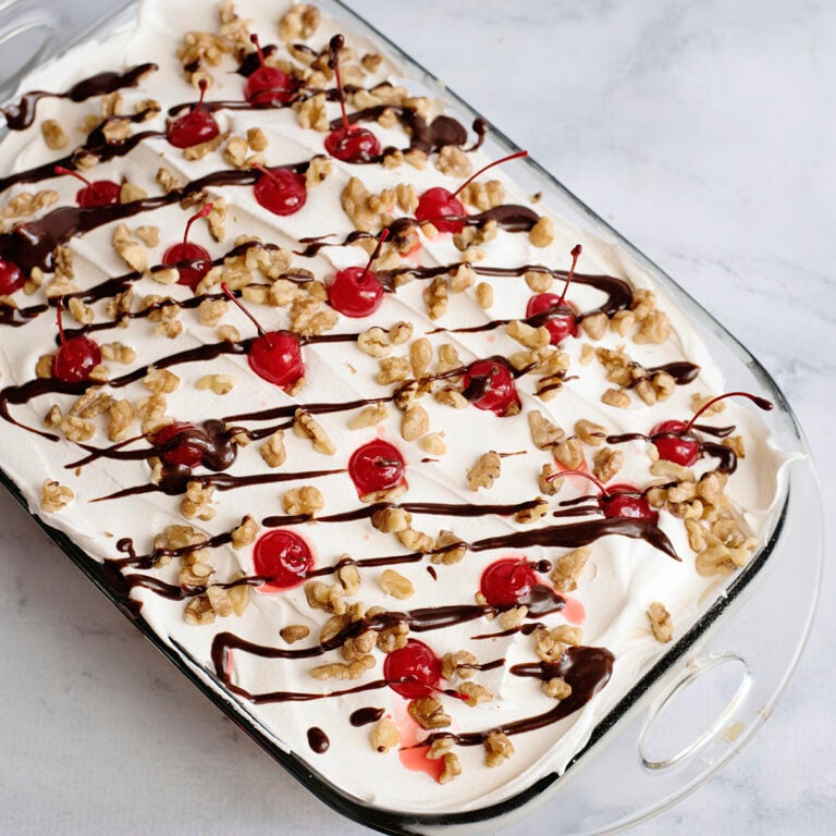 Banana Split Dessert in glass dish topped with cherries and drizzled with chocolate syrup.