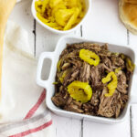 Shredded Italian Beef in white bowl with sliced sliced banana peppers on top
