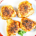 Four Cooked Chicken Thighs on white plate on top of red plaid napkin