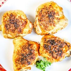 Four Cooked Chicken Thighs on white plate on top of red plaid napkin