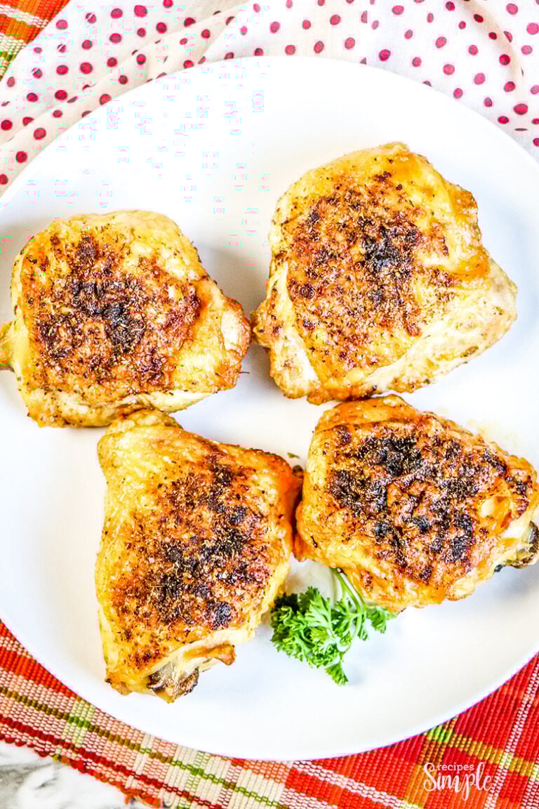 Four Cooked Chicken Thighs on white plate on top of red plaid napkin