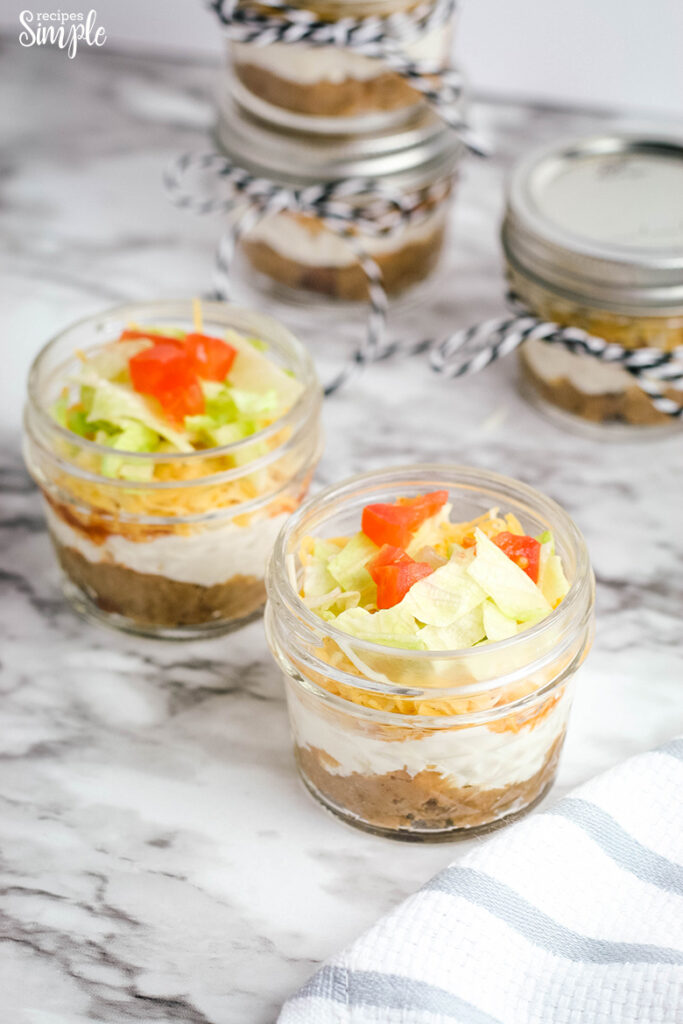 Layers of refried beans, sour cream, cream cheese, tomotes, lettuce and cheese in small mason jars