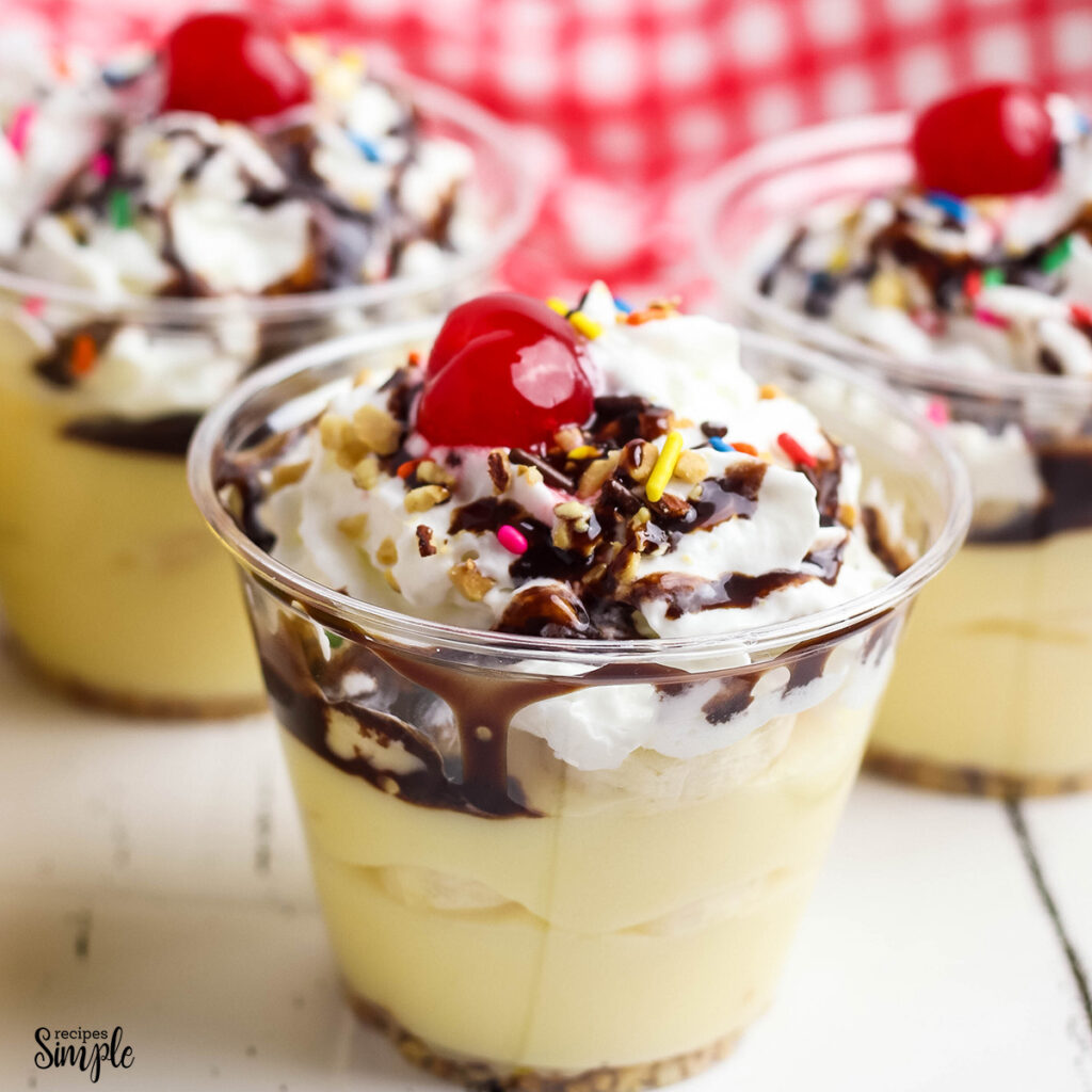 Banana Split Pudding in cups topped with sprinkles and cherry on top