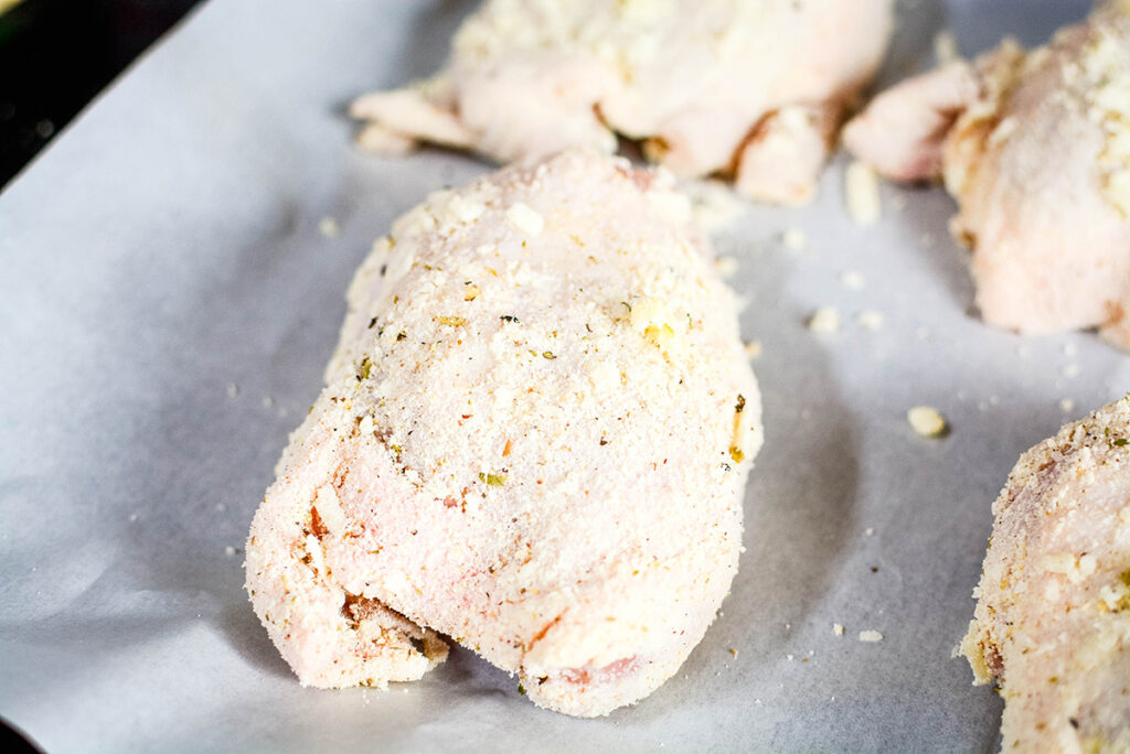 Chicken Thighes coated with seasoning and cheese on baking sheet