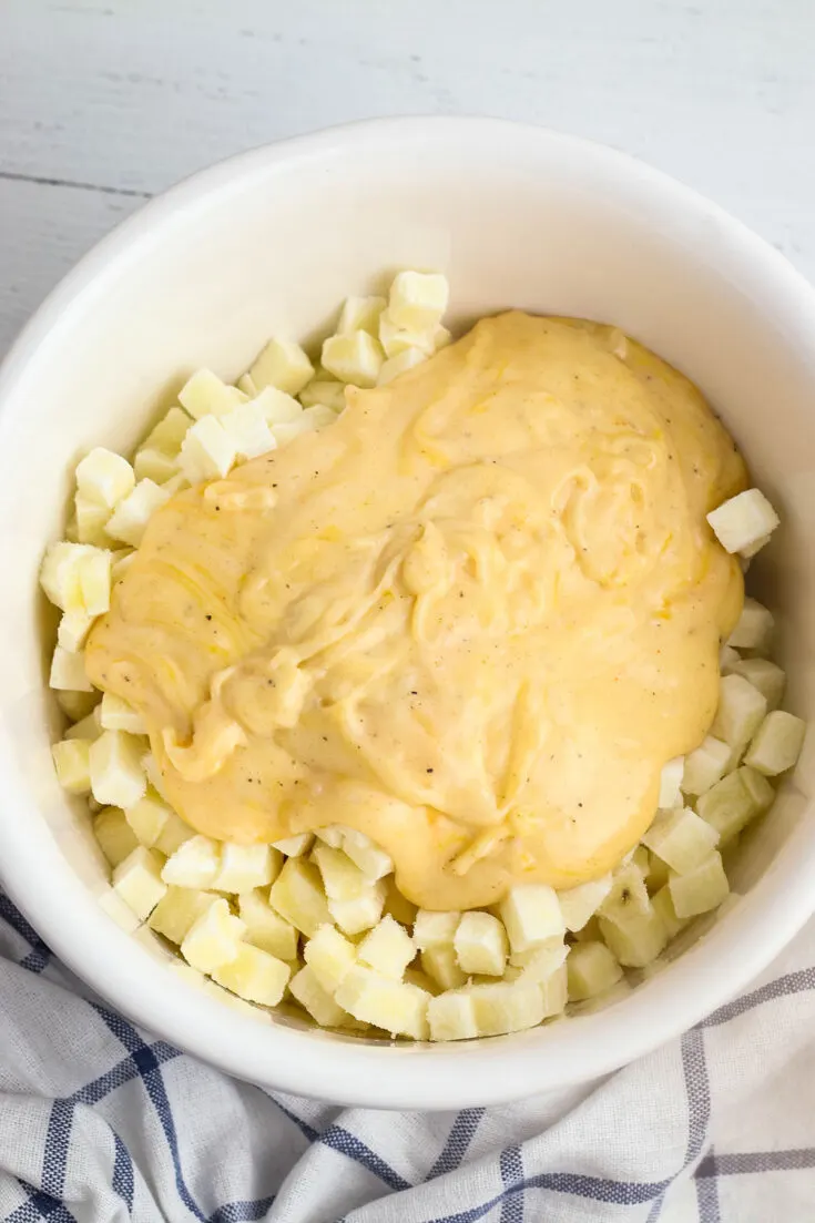 Cheese mixture added to diced potatoes in bowl