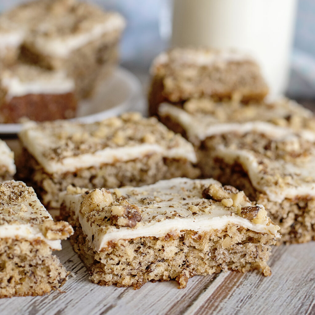 Banana Nut Bars with cream cheese frosting topped with crumbled walnuts on wood counter