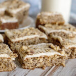 Banana Nut Bars with cream cheese frosting topped with crumbled walnuts on wood counter