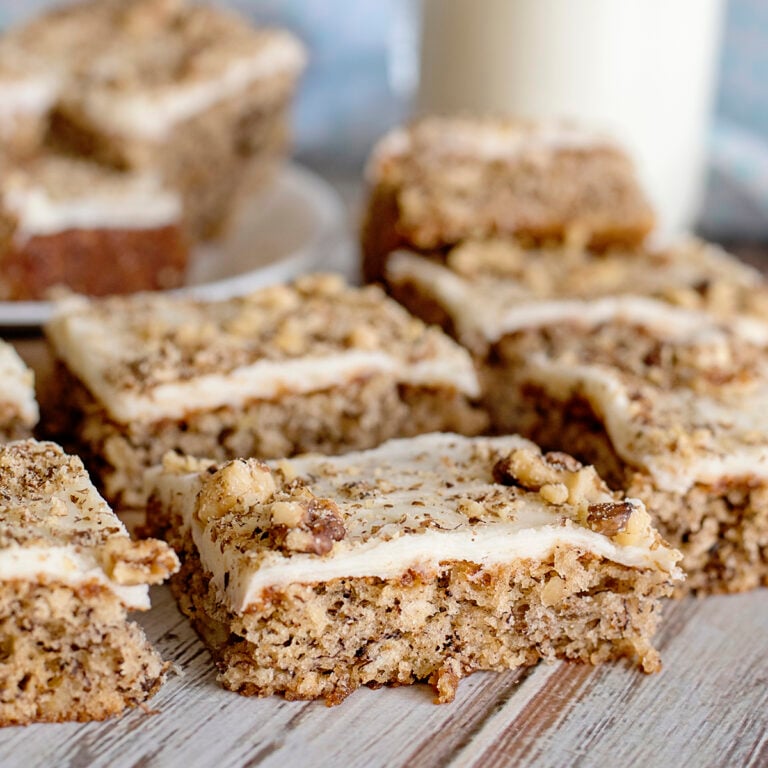 Banana Nut Bars with cream cheese frosting topped with crumbled walnuts on wood counter