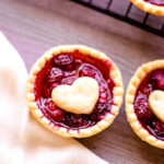 Two Mini Raspberry Tarts with heart shaped center on wood counter