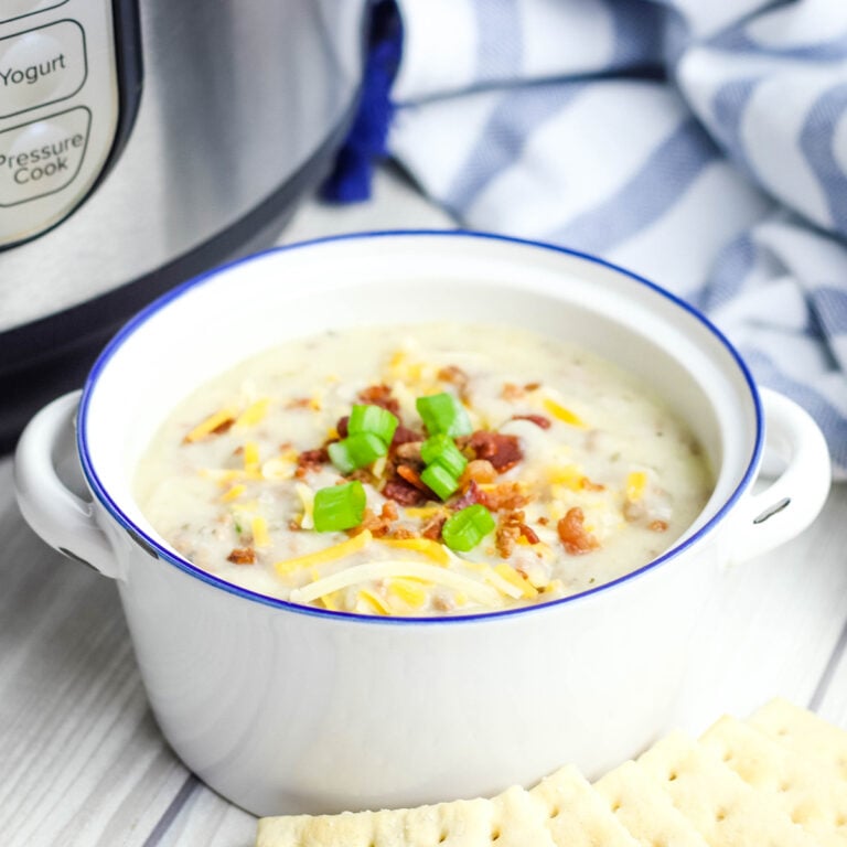 Cheeseburger soup served in white bowl topped with green onions and bacon crumbles with saltine crackers.