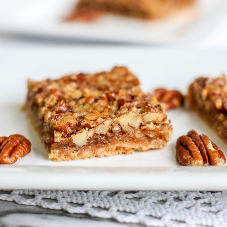 Pecan Pie Bar on white plate with pecan halves placed around it.