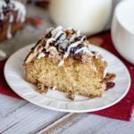Slice of Cranberry Pecan Upside Down Coffee Cake on white plate on wood counter with red napkin.