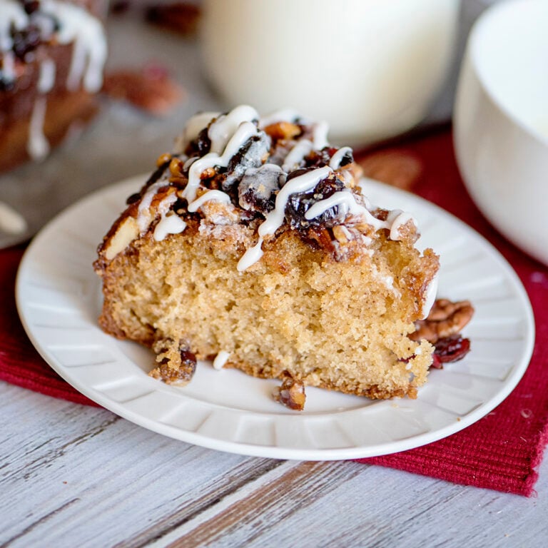 Slice of Cranberry Pecan Upside Down Coffee Cake on white plate on wood counter with red napkin.
