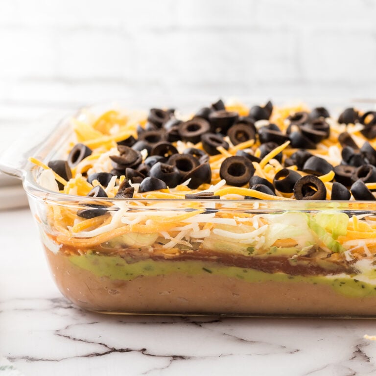 7 layer bean dip in glass serving dish on marble counter.