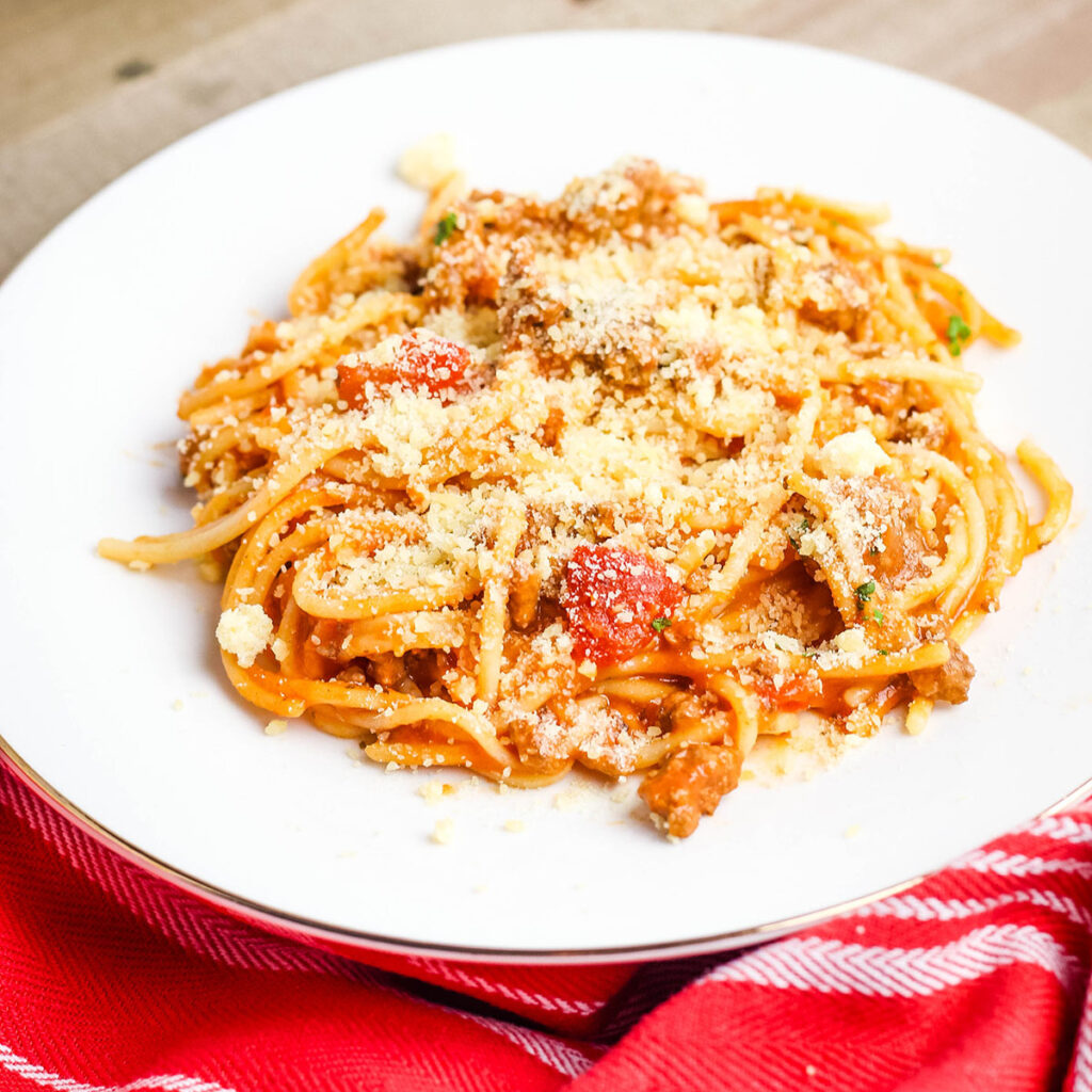 Spaghetti topped with Parmesan cheese on white plate.