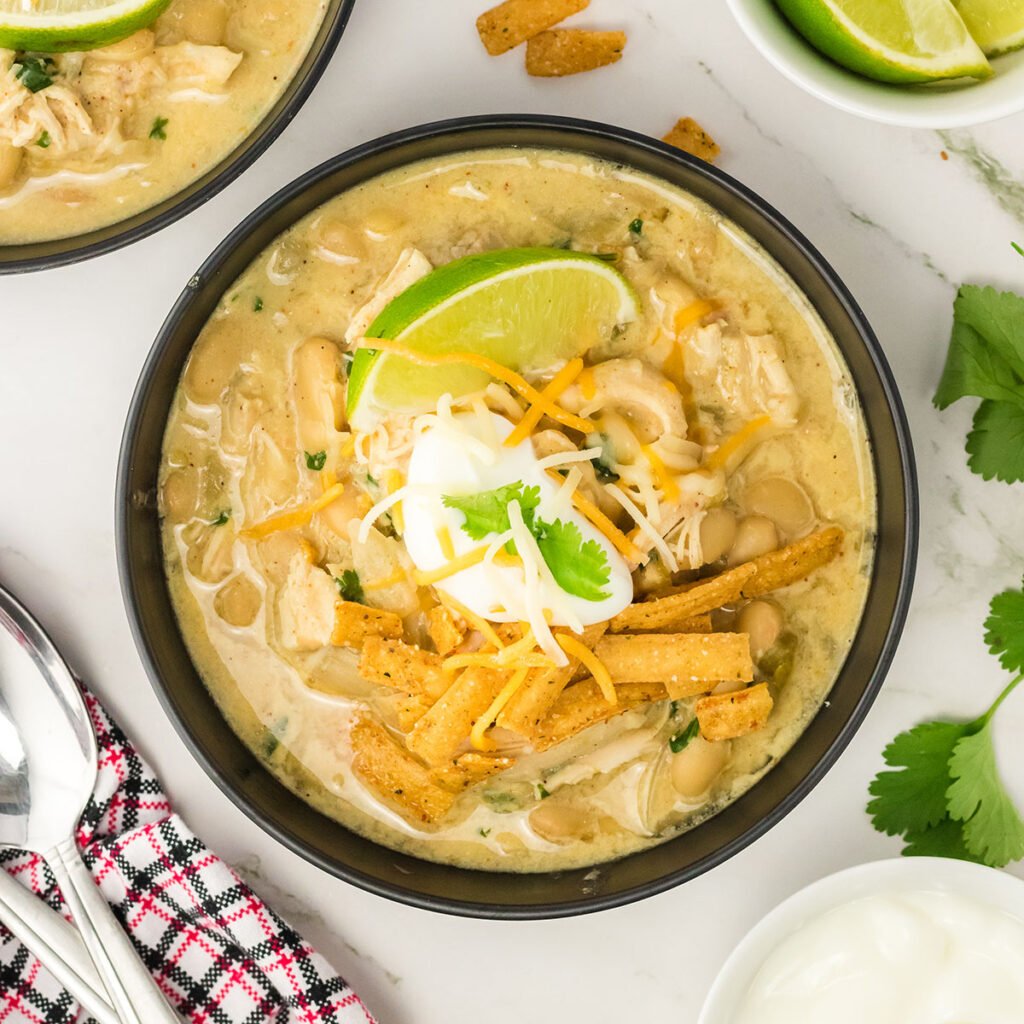 White Chicken Chili in black bowl topped with tortilla, sour cream and line wedge.