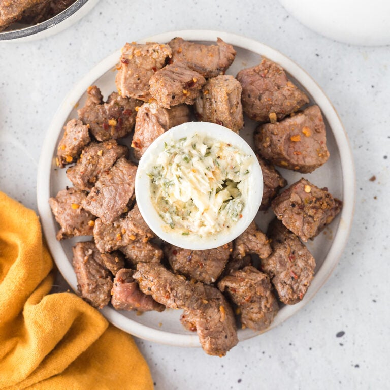 Steak Bites on white serving plate with placed around garlic butter bowl.