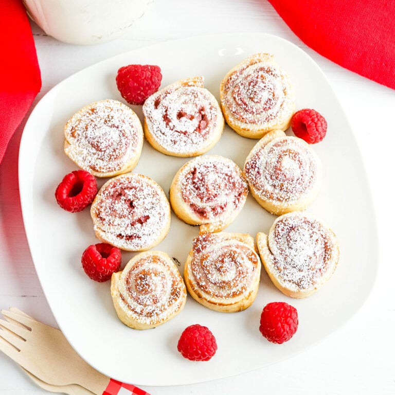 Nine Raspberry Pinwheels on white plate with fresh raspberries.