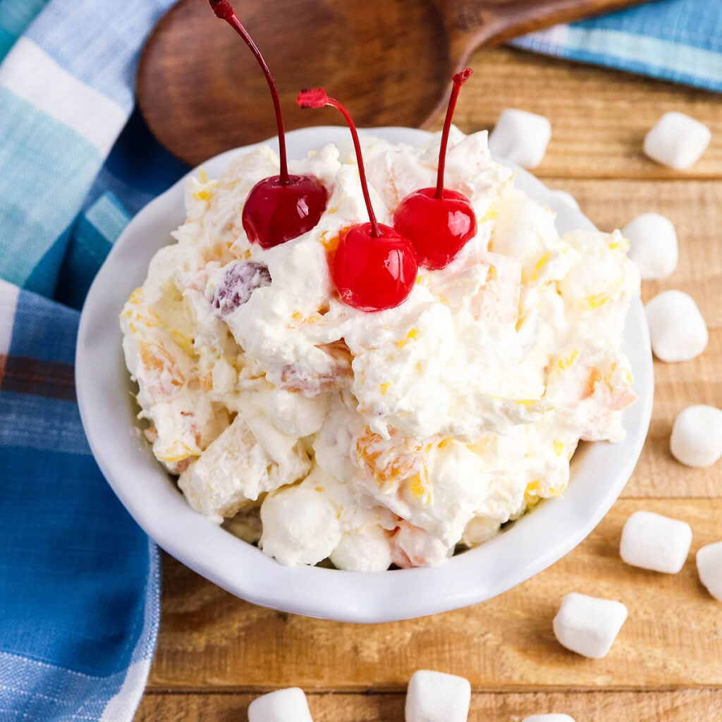 Marshmallow Fruit Salad in white serving dish topped with cherries.