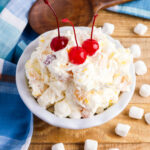 Marshmallow Fruit Salad in white serving dish topped with cherries.