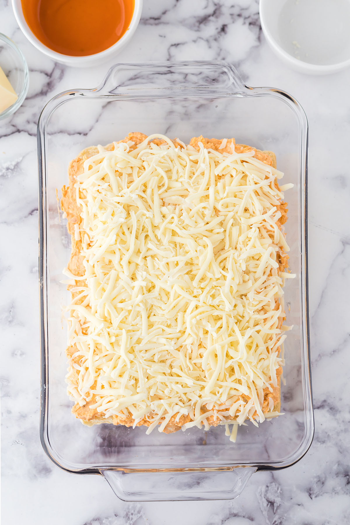 Chicken filling and cheese added to bottom of rolls in glass baking dish.