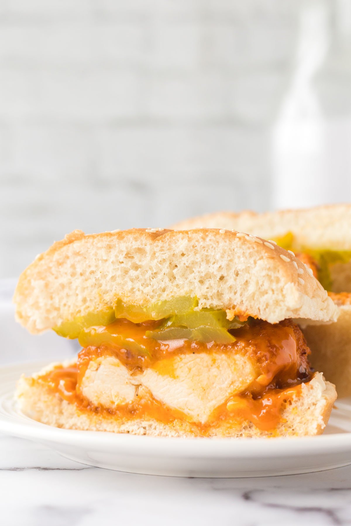 Buffalo Chicken Sandwich cut in half on bun with pickles.