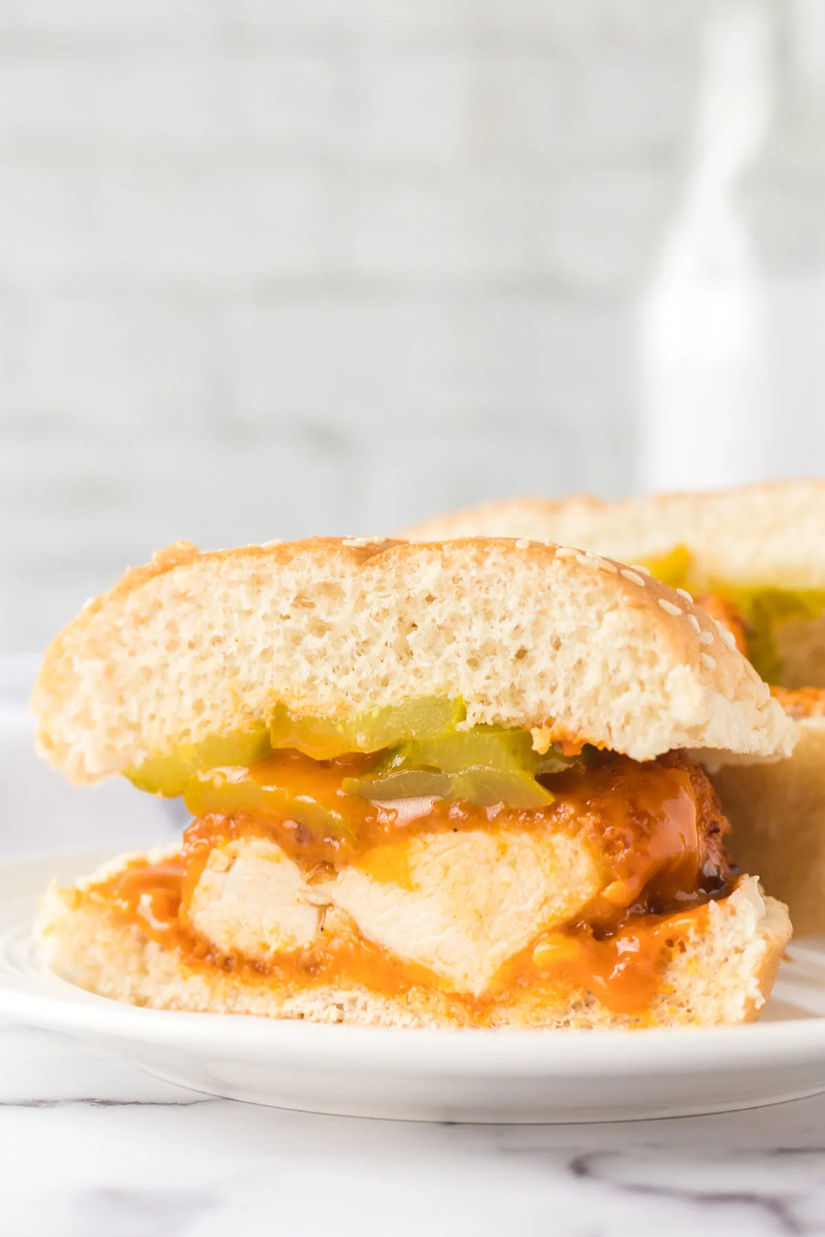 Buffalo Chicken Sandwich cut in half on bun with pickles.