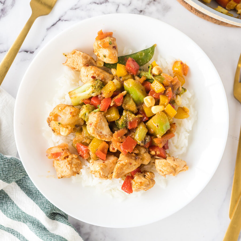 Chicken Stir Fry served over rice on white plate.