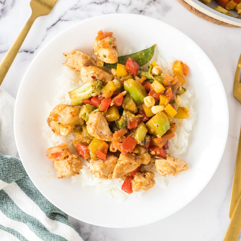 Chicken Stir Fry served over rice on white plate.