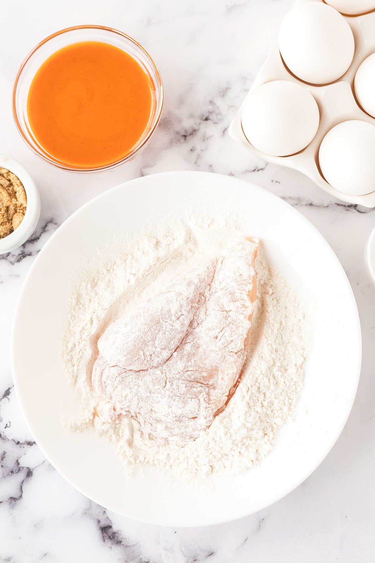 Chicken coated in flour in white bowl.