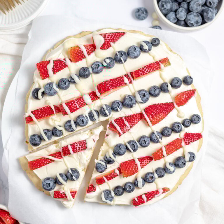 Fruit Pizza with white frosting decorated with strawberries and blueberries for 4th of July.