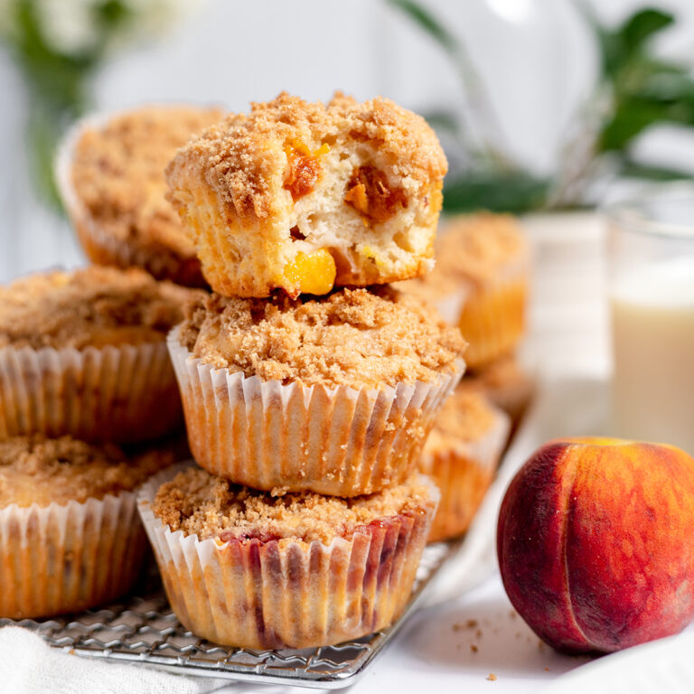 Peach Muffins stacked on wire rack with bite taken out of muffin on top.
