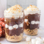 Two S'mores Parfaits in glass jars topped with whipped cream.