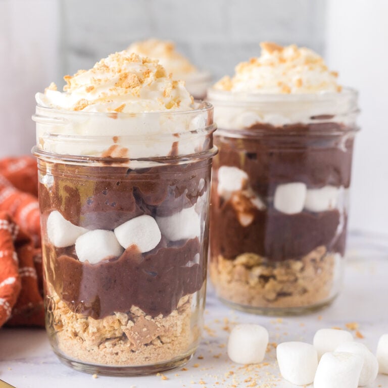 Two S'mores Parfaits in glass jars topped with whipped cream.