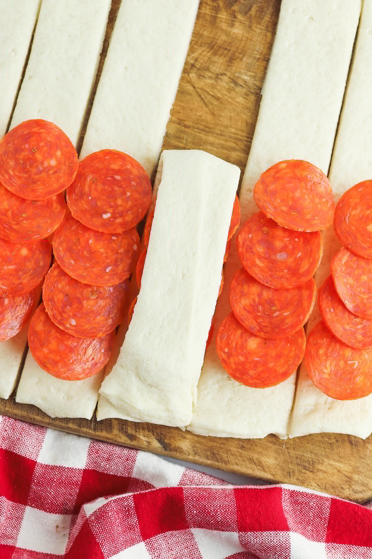 Folding the top of each pizza dough over the pepperoni and cheese.