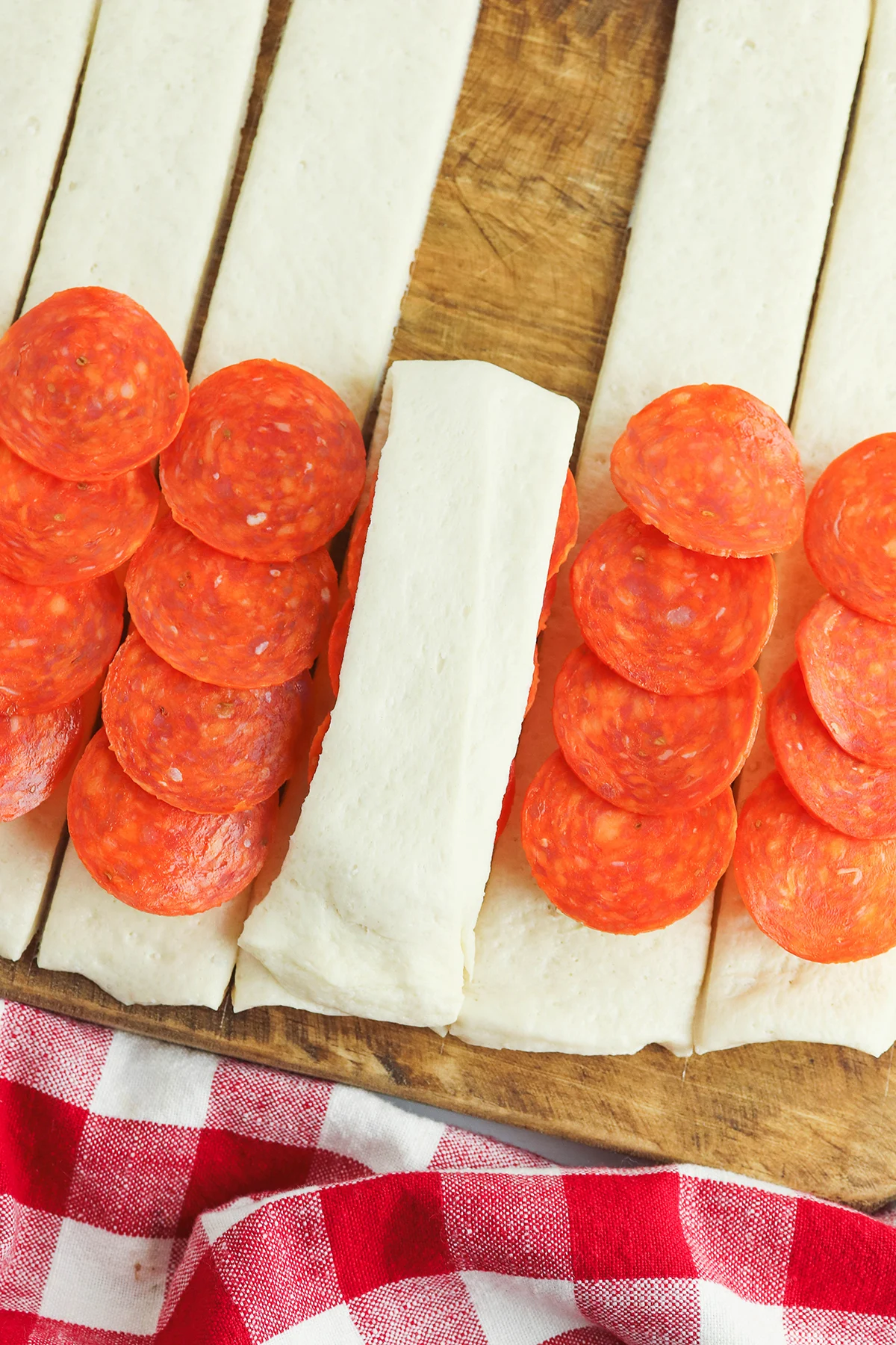 Folding the top of each pizza dough over the pepperoni and cheese.
